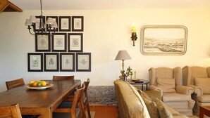 A dining area with a wooden table and chairs, a sofa, and a wall with framed pictures.