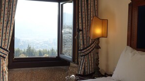 A hotel room with a large window, a bed, a nightstand, and a lamp.