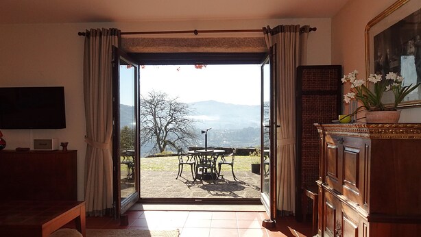 A room with a TV, a sofa, a dining table with chairs, a cabinet, and a view of mountains through an open door.