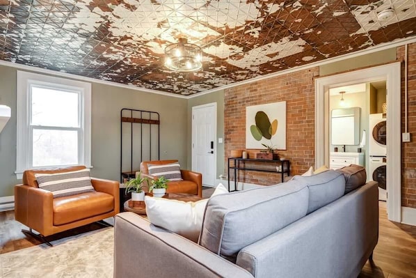 A living room with a brick wall, a large sofa, a leather armchair, and a coffee table with plants. - From HGTV! Marigold Suite in county farmhouse (Prince Edward)