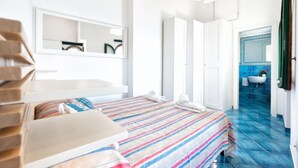 A modern hotel room with a bed, a bedside table, a mirror, and a bathroom visible through an open door.