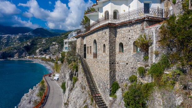 A stone building with a balcony overlooking a coastal road.
