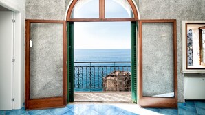 A room with a large arched doorway leading to a balcony with a view of the sea.