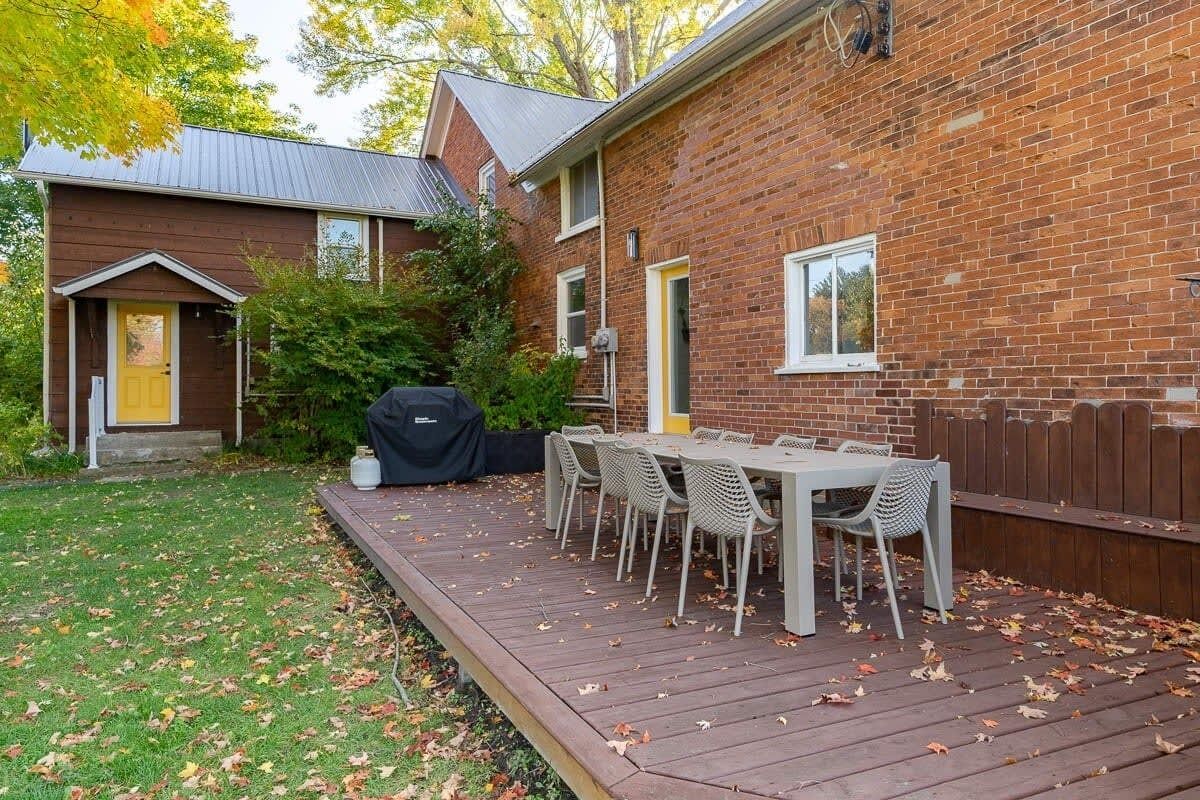 A backyard with a wooden deck, a barbecue grill, and a dining table with chairs.