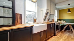Une cuisine moderne avec des meubles de couleur sombre, un plan de travail en bois, un évier blanc et un four.