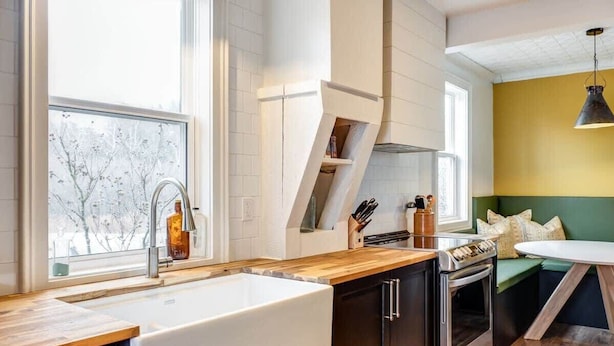 Une cuisine moderne dotée d’un plan de travail en bois, d’appareils électroménagers en acier inoxydable et d’une fenêtre offrant une vue sur des arbres couverts de neige.