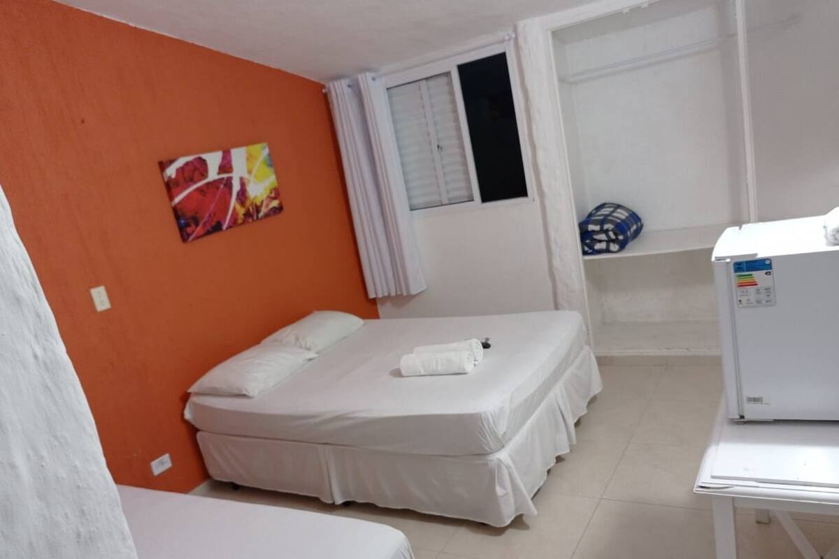 Una habitación con dos camas, un escritorio blanco, un refrigerador y una ventana con cortinas.