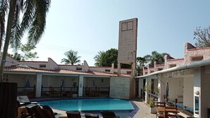 A pool area with lounge chairs and a tall structure. - Tropical Pousada (Guarujá)
