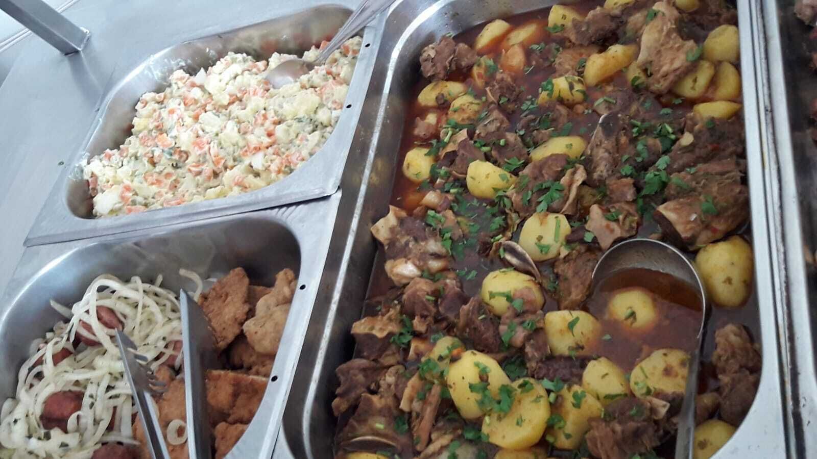 Un bufé con diversos platos, incluyendo carne, papas y una ensalada.