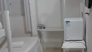 A small, sparsely furnished room with a bunk bed, a small table, and a refrigerator. - Tropical Pousada (Guarujá)