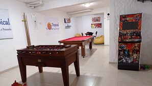 A pool table, foosball table, and a foosball machine in a room with white walls and tiled flooring. - Tropical Pousada (Guarujá)