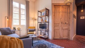 Ein gemütliches Wohnzimmer mit einer Couch, einem Couchtisch, einem Fernseher auf einem Regal und einer Holztür.