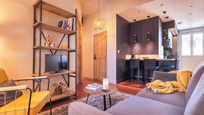 Ein modernes Wohnzimmer mit einer Couch, einem Bücherregal, einem Fernseher und einem Essbereich mit Tisch und Stühlen.