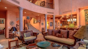 A spacious lobby with a grand staircase, a cozy seating area, and a kitchen visible in the background. - Beachfront 5 BR Villas del Mar 461 fts. Private Pool, Hot Tub, WiFi + Much More! (Los Cabos)