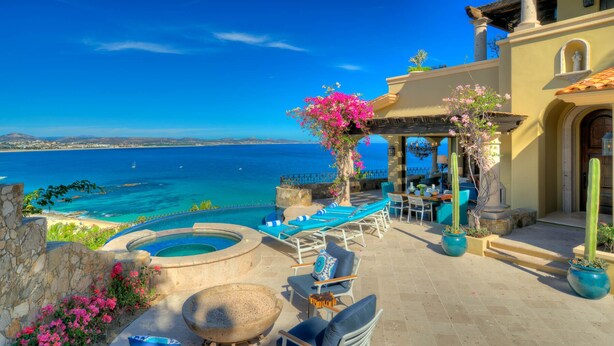 Un espacio al aire libre con sol, piscina, sillones de descanso y vistas al mar.