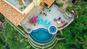 Vista aérea de un complejo turístico con una piscina circular, zonas de estar al aire libre y un porche cubierto.