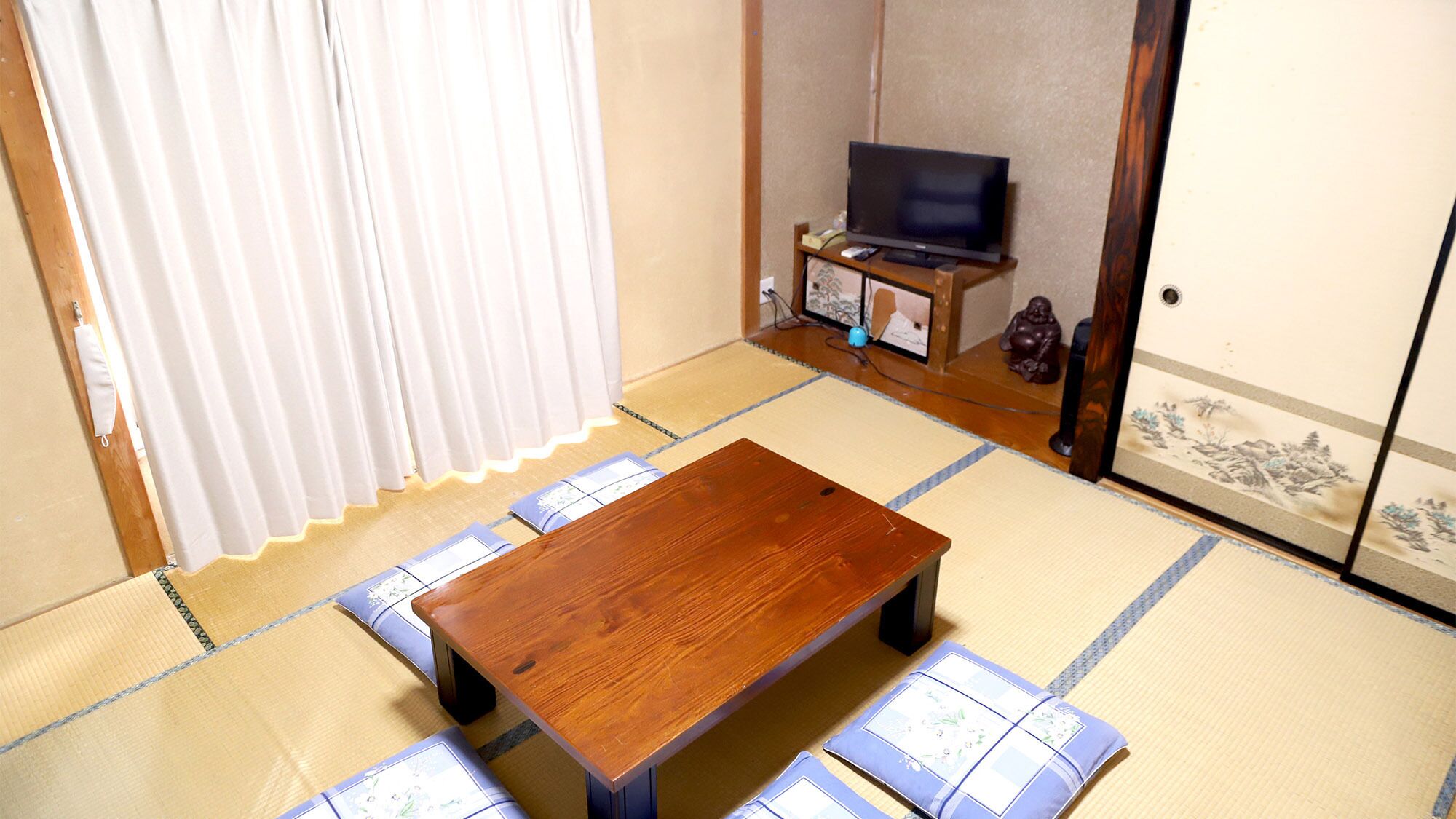 Una habitación con esteras de tatami, una mesa de madera, un televisor y un puertas correderas.