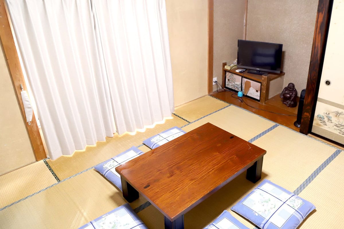 Una habitación con esteras de tatami, una mesa de madera, un televisor y un puertas correderas.
