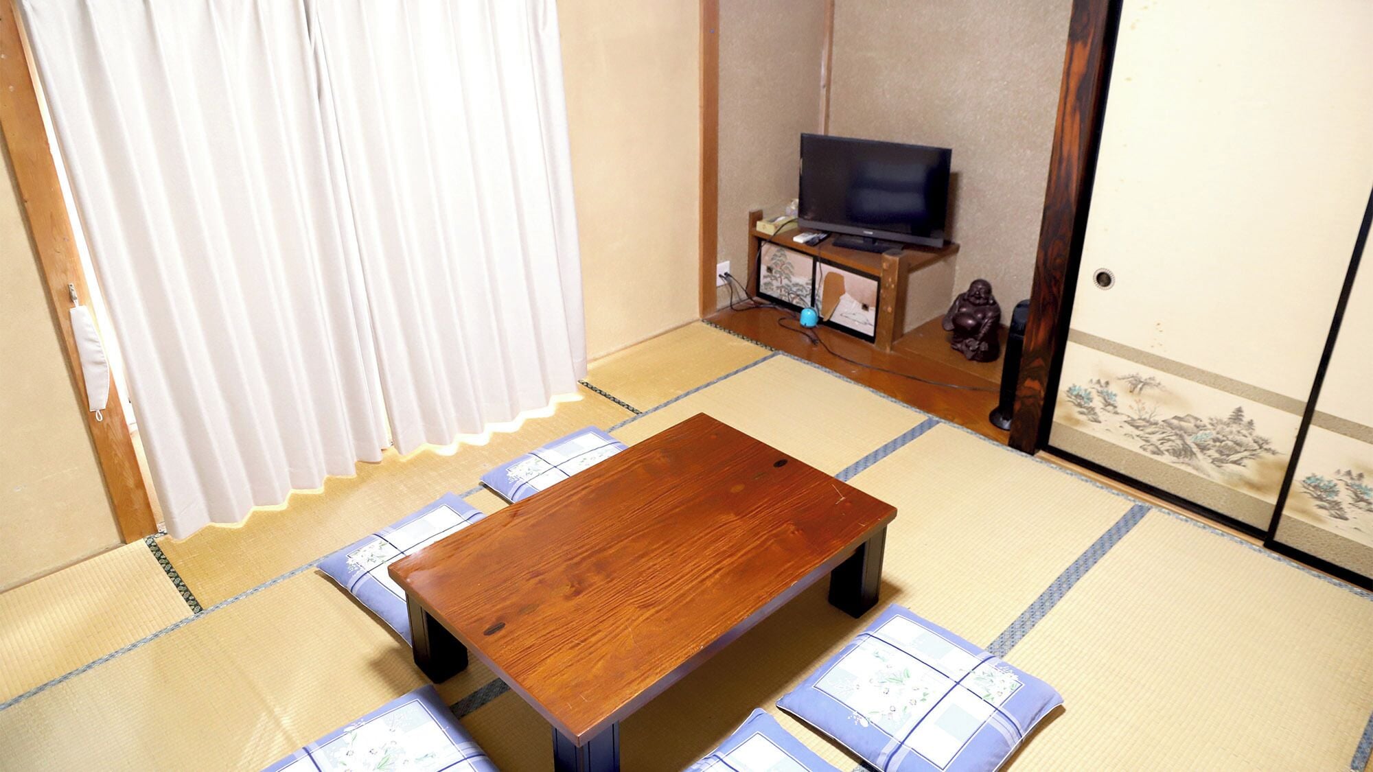 A tatami mat room with a wooden table, a television, and a wardrobe.