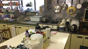 Una cocina con estufa, ollas, cafetera y distintos utensilios de cocina.