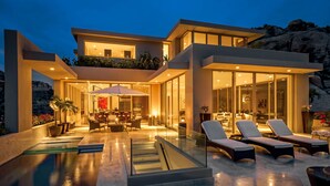 Una moderna casa a due piani con piscina, area salotto esterna e ampie finestre.