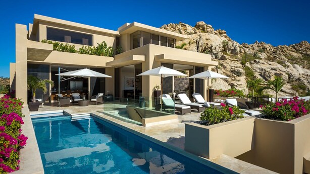 Una casa moderna con piscina, area relax all'aperto e vista su un paesaggio roccioso.