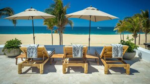 A beachside lounge with wooden lounge chairs and beige umbrellas, overlooking a sandy beach and the ocean. - 2 FREE NIGHTS IN CABO at Villa Pacifica! (Cabo San Lucas)
