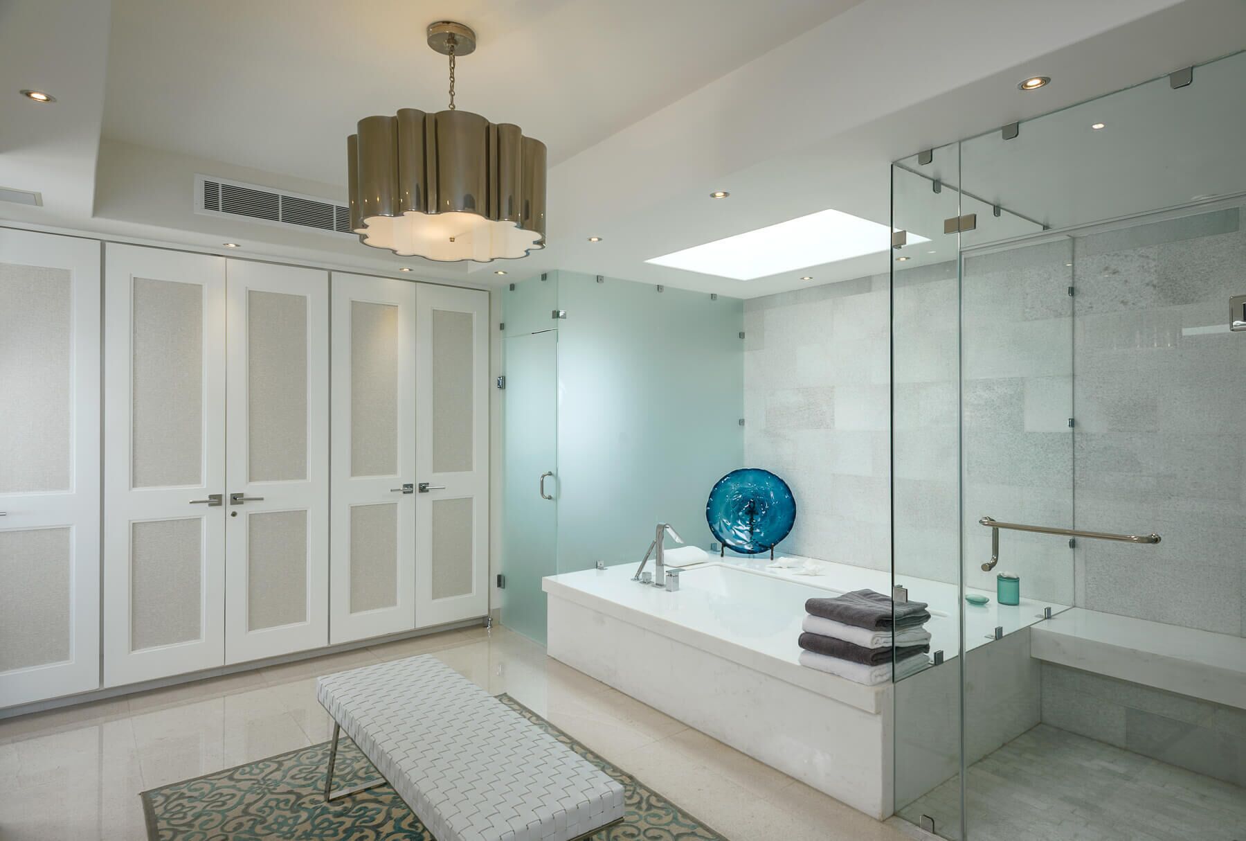 Een moderne badkamer met een glazen douchecabine, een vrijstaand bad en een bankje.