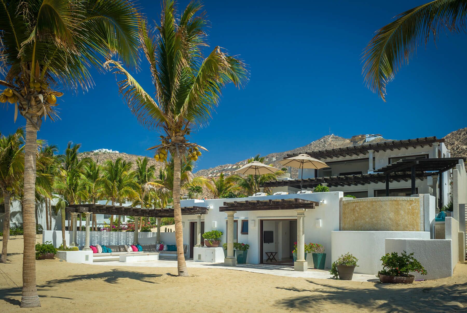 Un resort con spiaggia sabbiosa, palme e un edificio bianco con veranda coperta.