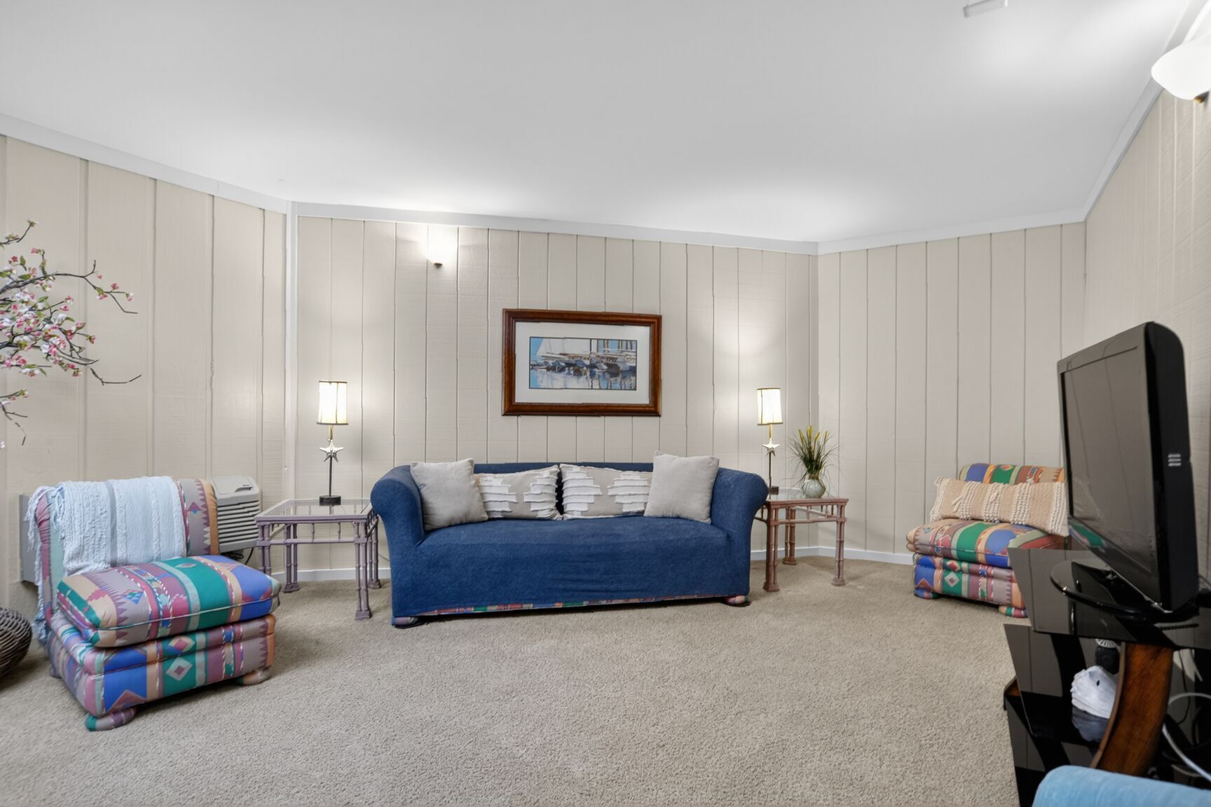 A living room with a blue sofa, two armchairs, a television, and a framed picture on the wall.