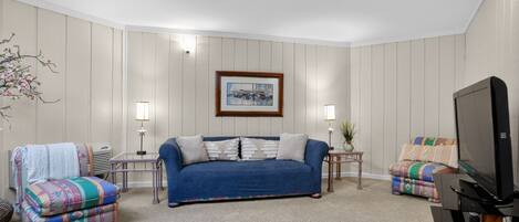 A living room with a blue sofa, two armchairs, a television, and a framed picture on the wall.