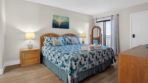 Habitación de hotel con cama, mesitas de noche, espejo y vista al mar a través de una ventana.