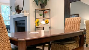 A dining area with a wooden table, woven chairs, and a bench. A chandelier hangs above, and a potted plant is on the wall.