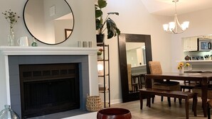 A living room with a fireplace, a dining area with a table and chairs, and a kitchen area with cabinets and appliances.