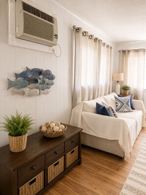 Une chambre à coucher comprenant un lit, une table de chevet, une lampe, un climatiseur mural et un élément décoratif représentant des poissons, fixé au mur.