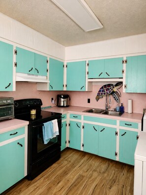 A kitchen with teal cabinets, a black stove, and a pink countertop. - Fore and Aft - Pet-friendly  (Myrtle Beach)