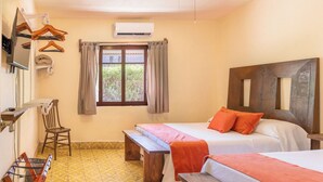 Een hotelkamer met twee bedden, een houten hoofdbord, een bankje, een stoel, een raam met gordijnen en een airconditioning.