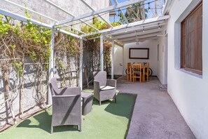 Un espace extérieur abrité comprenant deux fauteuils en osier, une table en bois et un écran de projection.