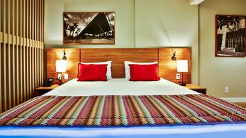 A hotel room with a large bed, red pillows, two bedside lamps, and a patterned rug.