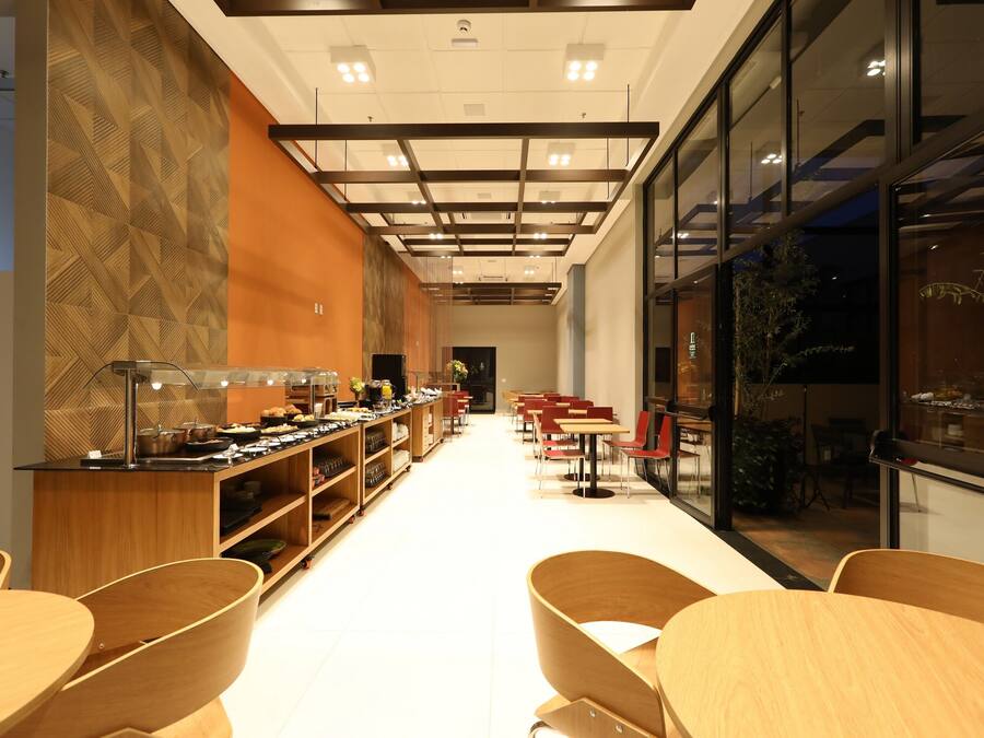 Un café moderne, doté de meubles en bois, d’un long comptoir où sont exposés divers produits, et offrant une vue dégagée grâce à de grandes fenêtres.