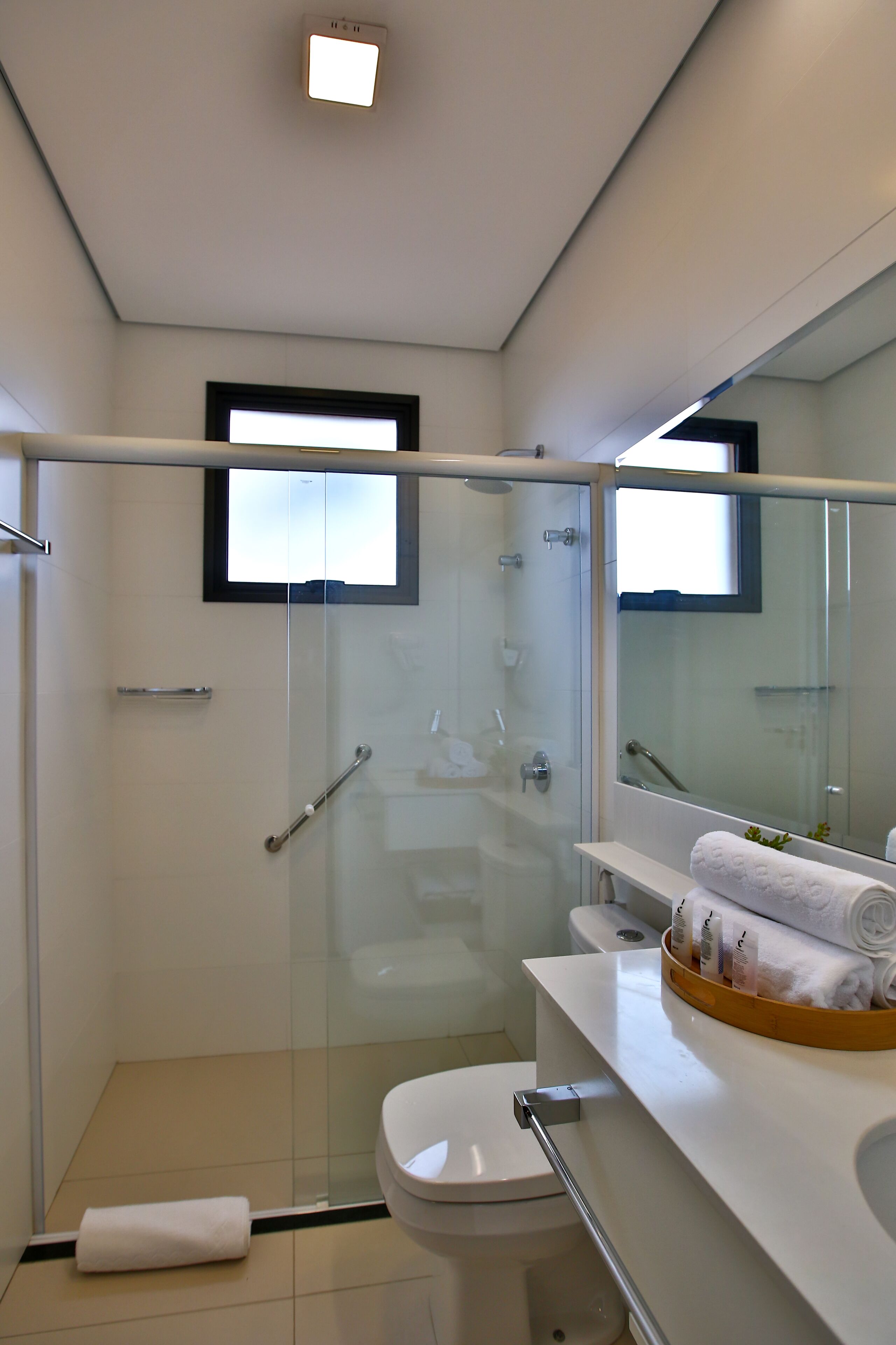 Ein modernes Badezimmer mit einer gläsernen Duschkabine, einer Toilette und einem Waschtisch mit Spiegel und Handtuchhalter.
