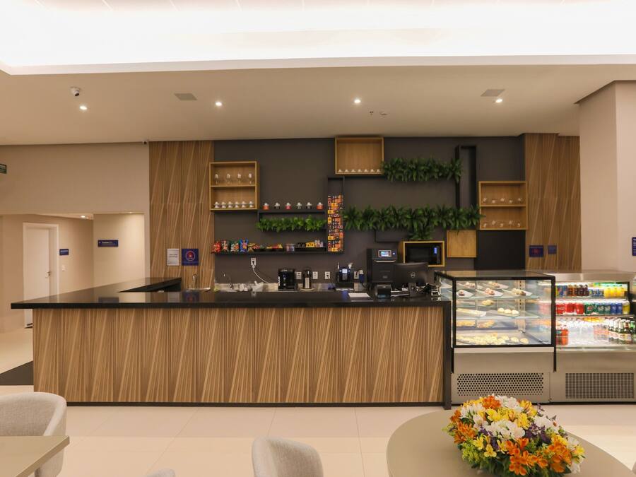 Zona de recepción con mostrador de madera, una vitrina con aperitivos y una pequeña composición floral.