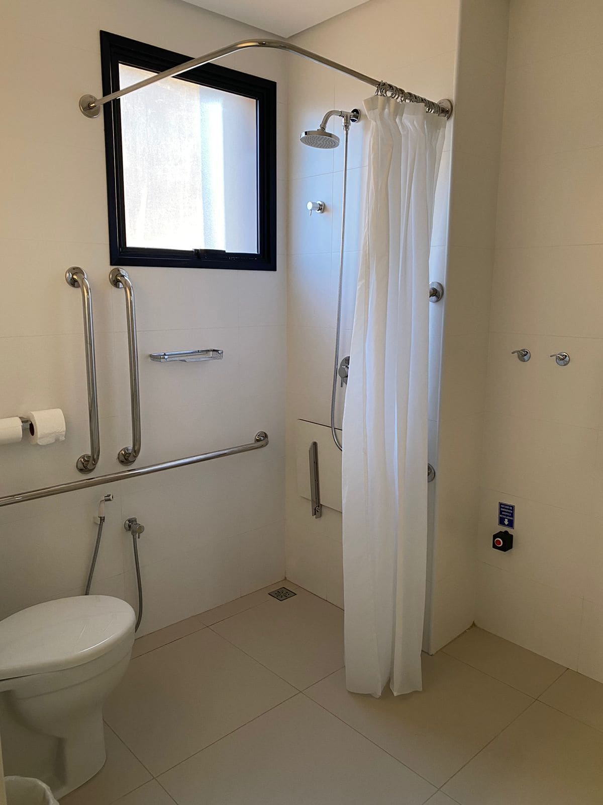 Un baño con inodoro, ducha con cortina y barras de apoyo.