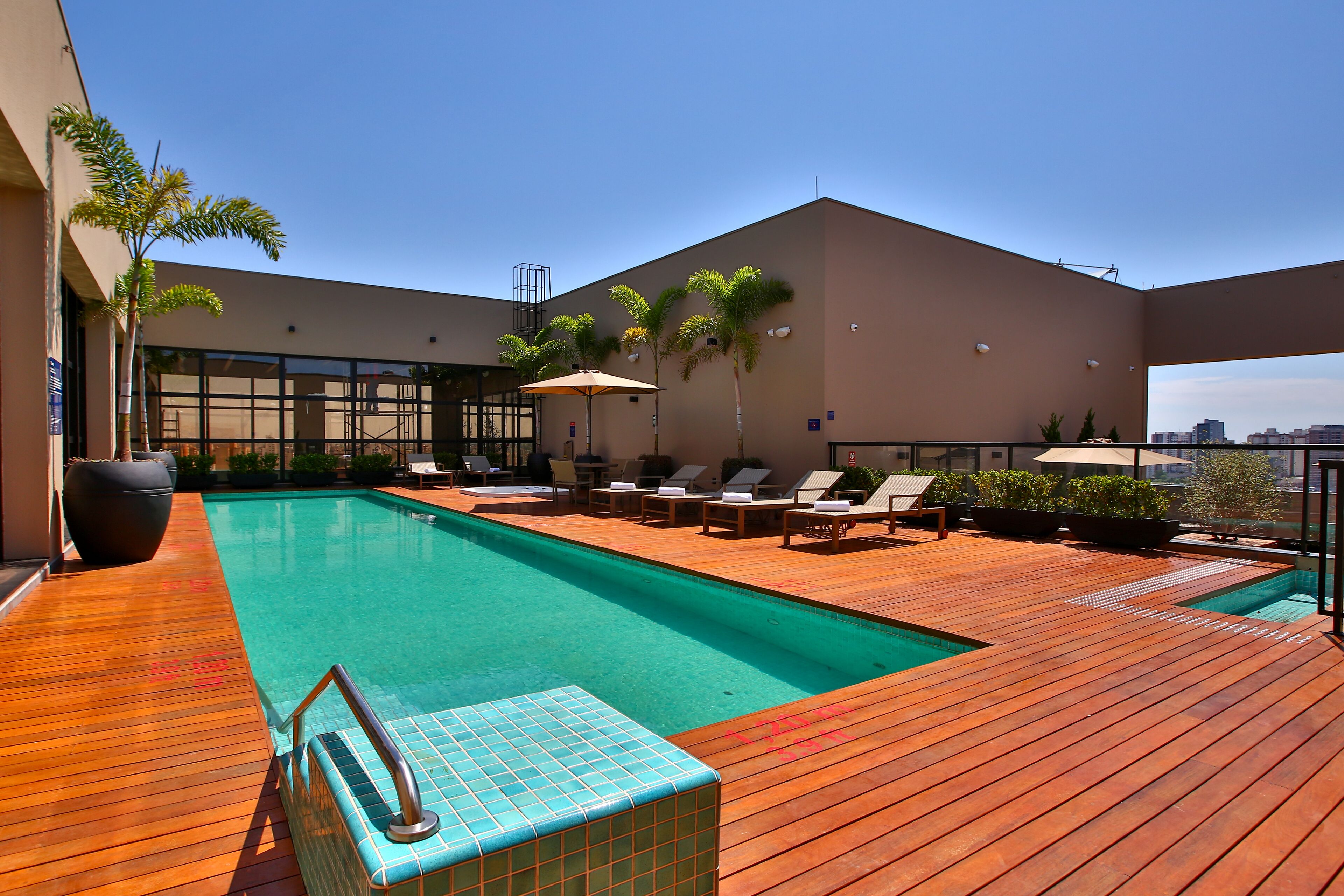 Zona de piscina en la azotea con terraza de madera, sillones de descanso y una piscina.