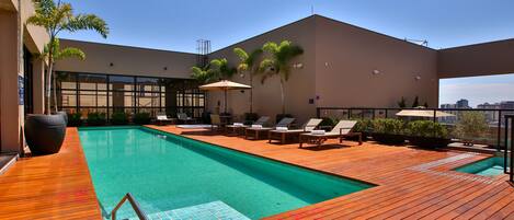 Zona de piscina en la azotea con terraza de madera, sillones de descanso y una piscina.