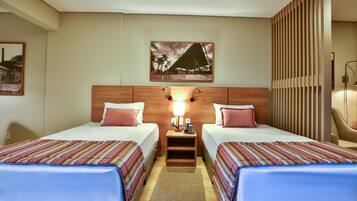 A hotel room with two beds, a nightstand with a lamp, a painting on the wall, and a wooden partition.