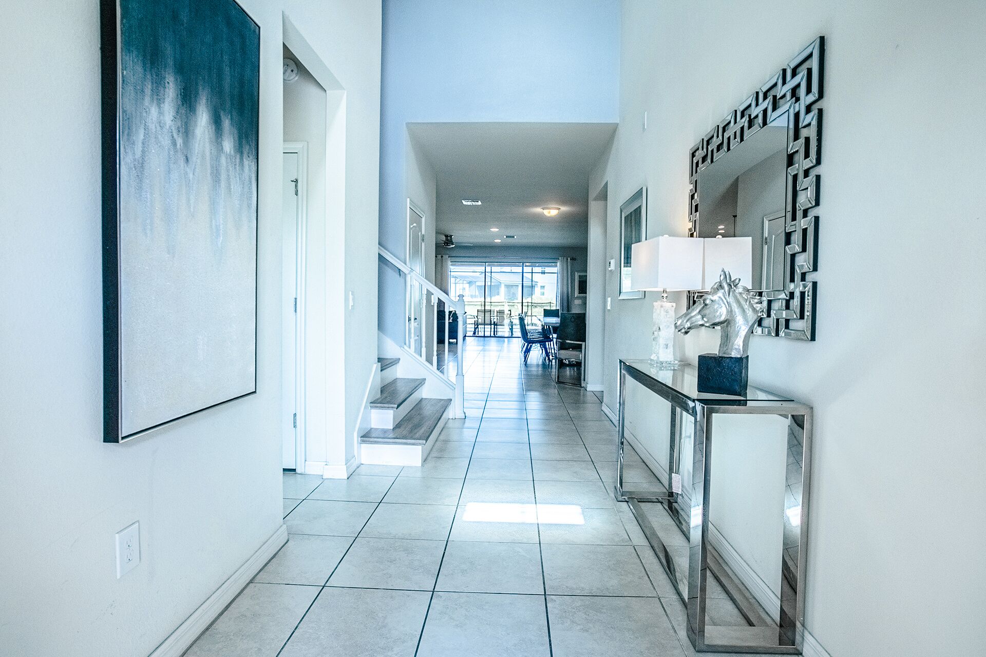 A modern hallway with a staircase, a dining area in the background, and a decorative horse head on a console table.