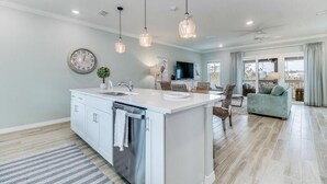 A modern kitchen with a central island, pendant lighting, a clock, and a view to the living area. - Beaches and Birdies, Lost Key Golf and Beach Resort (Pensacola)