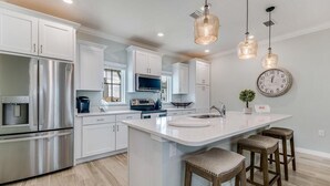 A modern kitchen with white cabinetry, stainless steel appliances, and a central island with bar stools. - Beaches and Birdies, Lost Key Golf and Beach Resort (Pensacola)