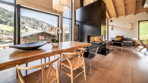 A modern interior with a wooden dining table, chairs, a fireplace, and large windows offering a scenic view. - NELCOTE - Design and luxury chalet with hot tub (Morzine)